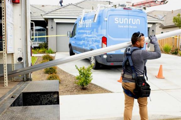 Sunrun solar installer carrying mounts with a Sunrun solar van at the back