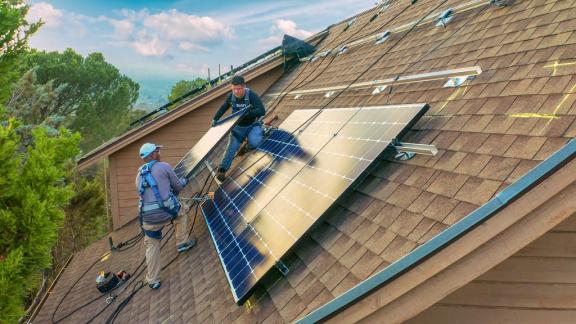 Sunrun solar installers moving a solar panel on the roof of a home.
