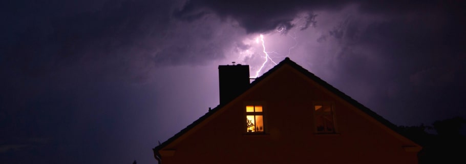lightning striking behind house with lights on