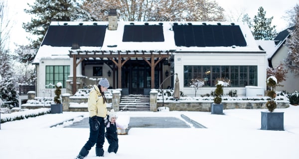 Family walking in snow in front of house with solar panels on roof