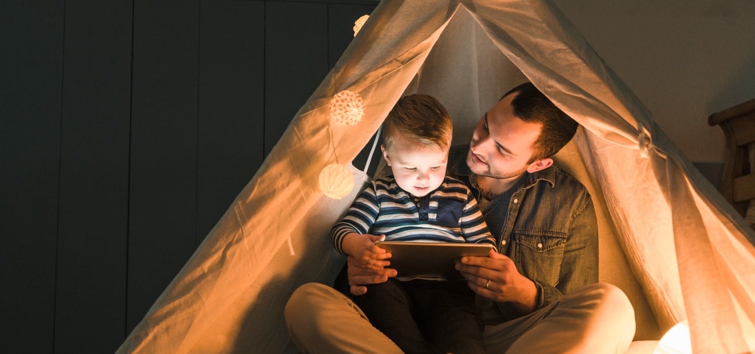 Father and infant son using a tablet inside a blanket fort