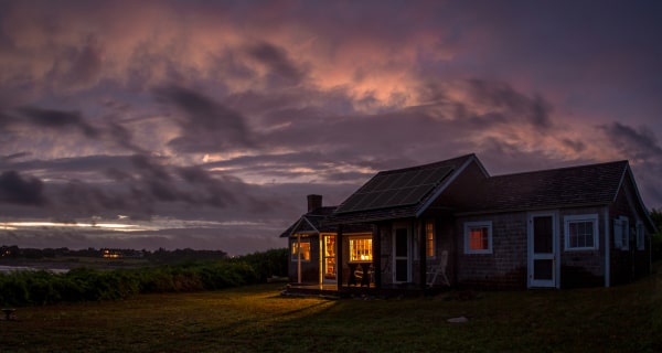 Home in meadow with lights on and storm in background