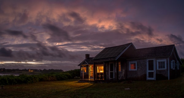 Home in meadow with lights on and storm in background 